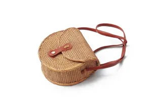 Detail view of the handcrafted round woven rattan crossbody bag with brown leather strap and buckle.