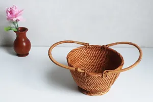 Detail view of a handcrafted woven rattan fruit basket with dual handles and stable base structure.