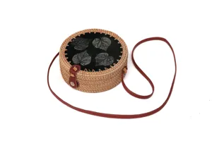 Runder geflochtener Rattan-Umhängetasche Detail mit bedrucktem Lederdeckel und Gurt.