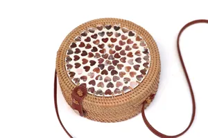 Runde gewebte Rattan-Umhängetasche mit Muschel-Herz-Muster und braunem Lederriemen.