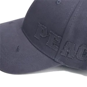 Detail op donkergrijze distressed honkbalpet met geborduurde PEACE letters en rafelranden.