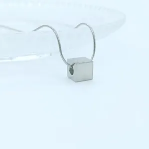 Minimalist silver cube pendant detail shot on delicate snake chain, modern geometric style.