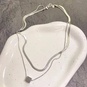 Close-up detail of double layer silver snake bone necklace with small square pendant on white tray.