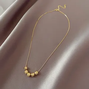 Détail de collier en acier titane perles dorées, breloques sphériques et chaîne délicate.