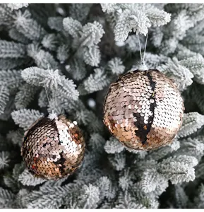 Primer plano detallado de bolas de Navidad con lentejuelas doradas en un árbol nevado.