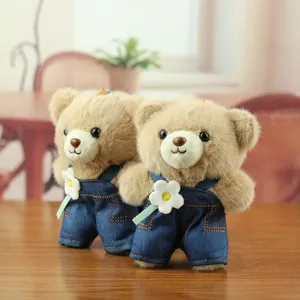 Adorable pendentif en peluche ours portant une salopette en jean avec fleur, gros plan.