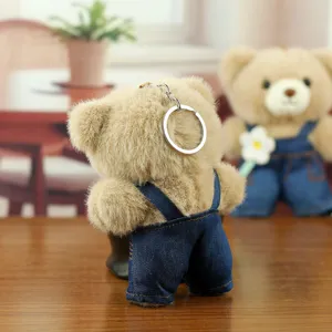 Gros plan de porte-clés ours en peluche mignon portant une salopette en jean sur table.
