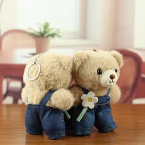 Gros plan sur le porte-clés en peluche mignon d'ours en salopette en denim avec une fleur.
