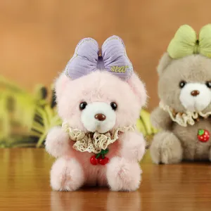 Close-up detail of cute pink plush bear pendant with purple bow and cherry decor for bags.