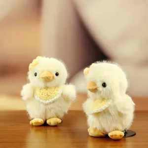 Primer plano del tierno pollito de peluche amarillo con babero tejido y detalle floral.
