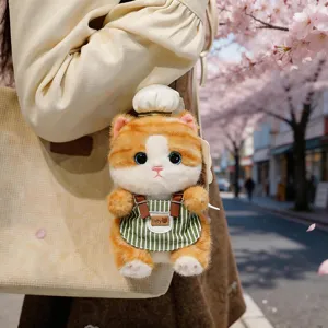 Primo piano di un ciondolo peluche gatto arancione con cappello da cuoco e grembiule su borsa.