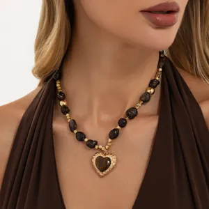 Close-up weergave van de vintage gouden hartjesketting met donkere kralenkettingdetails.