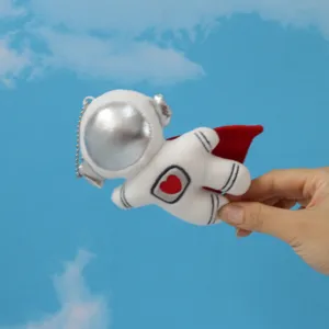 Detailaufnahme des Plüsch-Astronauten-Schlüsselanhängers mit silbernem Helm und rotem Umhang.