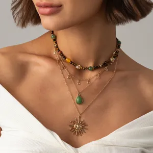 Détail de gros plan d'un ensemble de colliers dorés multicouches avec choker et pendentif soleil.