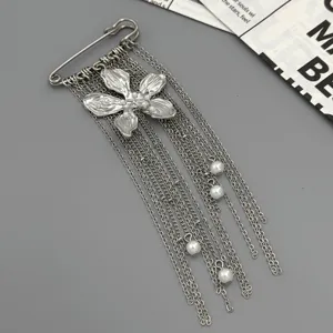Detailed view of the stylish metal safety pin brooch with hanging chains, floral pendant and pearl.