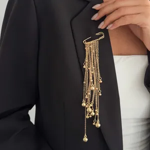 Gold-toned safety pin brooch featuring multi-chain tassel drops and bead charms worn on lapel.