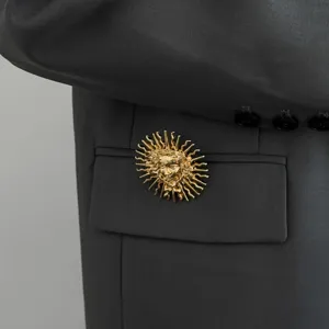 Detailed view of a gold baroque sun face brooch on a dark grey suit jacket, elegant accessory.