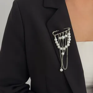 Detailed view of a silver safety pin brooch featuring dangling faux pearls and chic chains.
