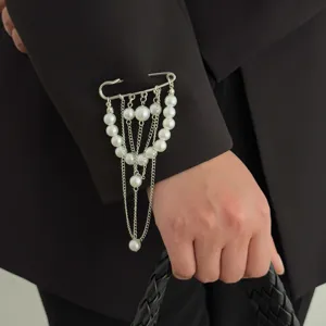 Close-up of a stylish pearl tassel safety pin brooch on black suit sleeve, elegant detail.