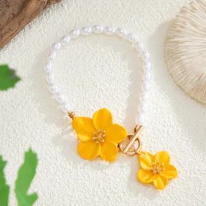 Detalle de tobillera bohemia con perlas falsas, flores amarillas pintadas y cierre de barra dorado.