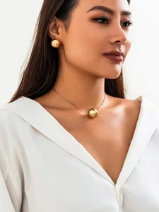Close-up detail of minimalist gold-tone spherical pendant necklace and matching round earrings.