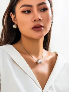 Closeup shot of minimalist silver metal snake bone chain with geometric round ball pendant.