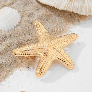 Close-up detail of the gold starfish hair clip showing textured metallic surface on sand.