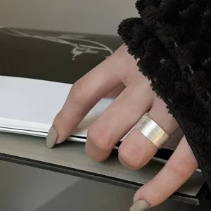 Closeup detail view of wide matte silver geometric open ring worn gracefully on index finger.