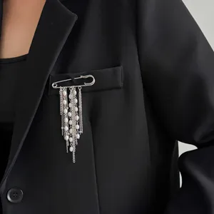 Close-up detail of elegant silver safety pin brooch with hanging pearls and chains for women.