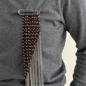 Dettaglio della spilla con nappe di perline e spilla di sicurezza con catene argento.