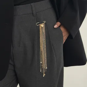 Close-up detail of a stylish multi-chain tassel brooch pin on grey trousers for elegant outfits.