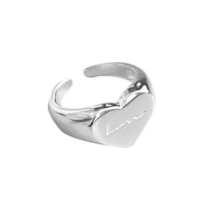 Close-up detail of a silver open ring with a cute heart face and engraved love script.