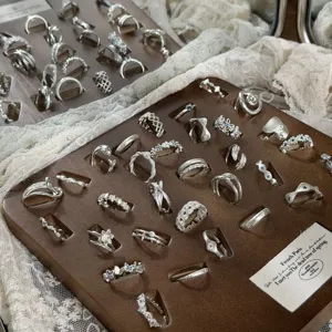 Close-up details of various minimalist silver rings displayed neatly on a vintage wooden tray.