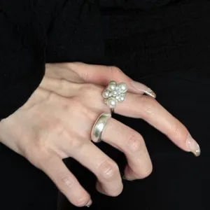 Detail shot of sweet imitation pearl and metal rings worn on hand, elegant design for daily wear.
