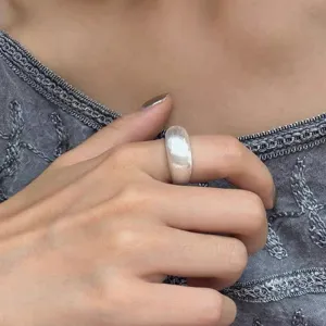 Close-up detail of a wide brushed silver ring worn on index finger, elegant minimalist design.