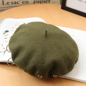 Close-up of military green wool beret with metal rings, punk vintage style hat detail view.