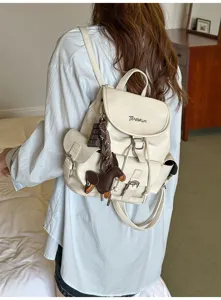 Detail view of stylish beige PU leather backpack with cute dog pendant and chocolate charm for women.