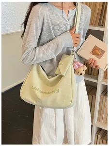Close-up of light green slouchy shoulder bag featuring cute bear charm and front flap pocket.
