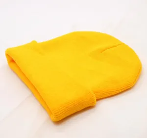 Yellow knitted beanie detail view, classic plain cuffed winter hat fabric close up.