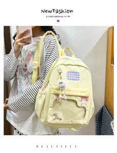 Cute milky yellow canvas backpack detail with transparent window, bow embroidery and furry pendant.