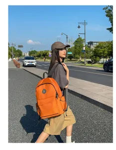 Detail shot of orange nylon backpack worn by model outdoors on street, casual style.