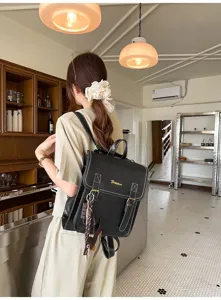 Black PU leather backpack detail showing white contrast stitching and flap design in a cafe setting.