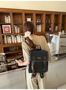 Detailed lifestyle view of black leather fashion backpack with contrast stitching in cafe setting.