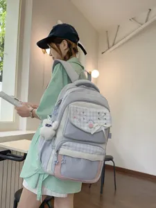 Detail view of the light blue plaid student backpack with cute embroidery and hanging doll decor.