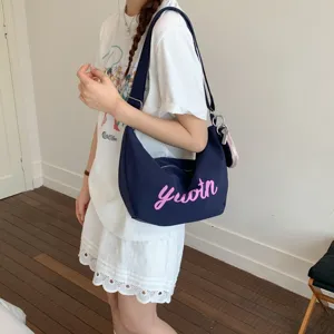 Detail view of a dark blue canvas shoulder bag with pink lettering and adjustable strap.