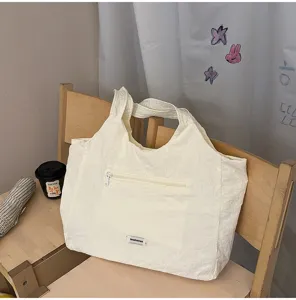 Detailopname van de gebroken witte gekreukte nylon tote bag met ritsvak aan de voorzijde en label.