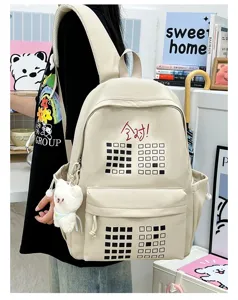 Detailed view of a casual beige student backpack with cute bear pendant and geometric pattern.