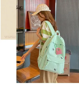Close-up detail view of the light green student backpack featuring cute embroidery and pockets.