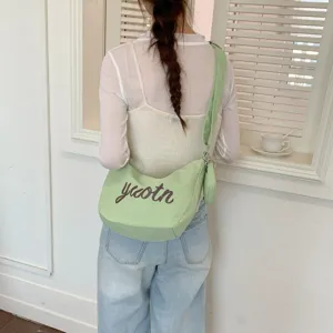 Detailed view of the light green canvas crossbody bag with letter print and wide strap.
