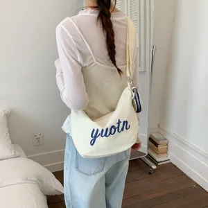 Canvas shoulder crossbody bag with blue letter print, casual everyday fashion detail shot.